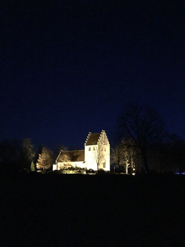 Natbillede af Næsbyhovedbroby Kirke. kirken er stærkt belyst med en dyb blå himmel som kontrast