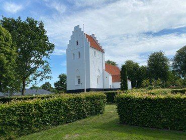 Næsbyhoved Broby kirke set udefra i sollys med lette skyer