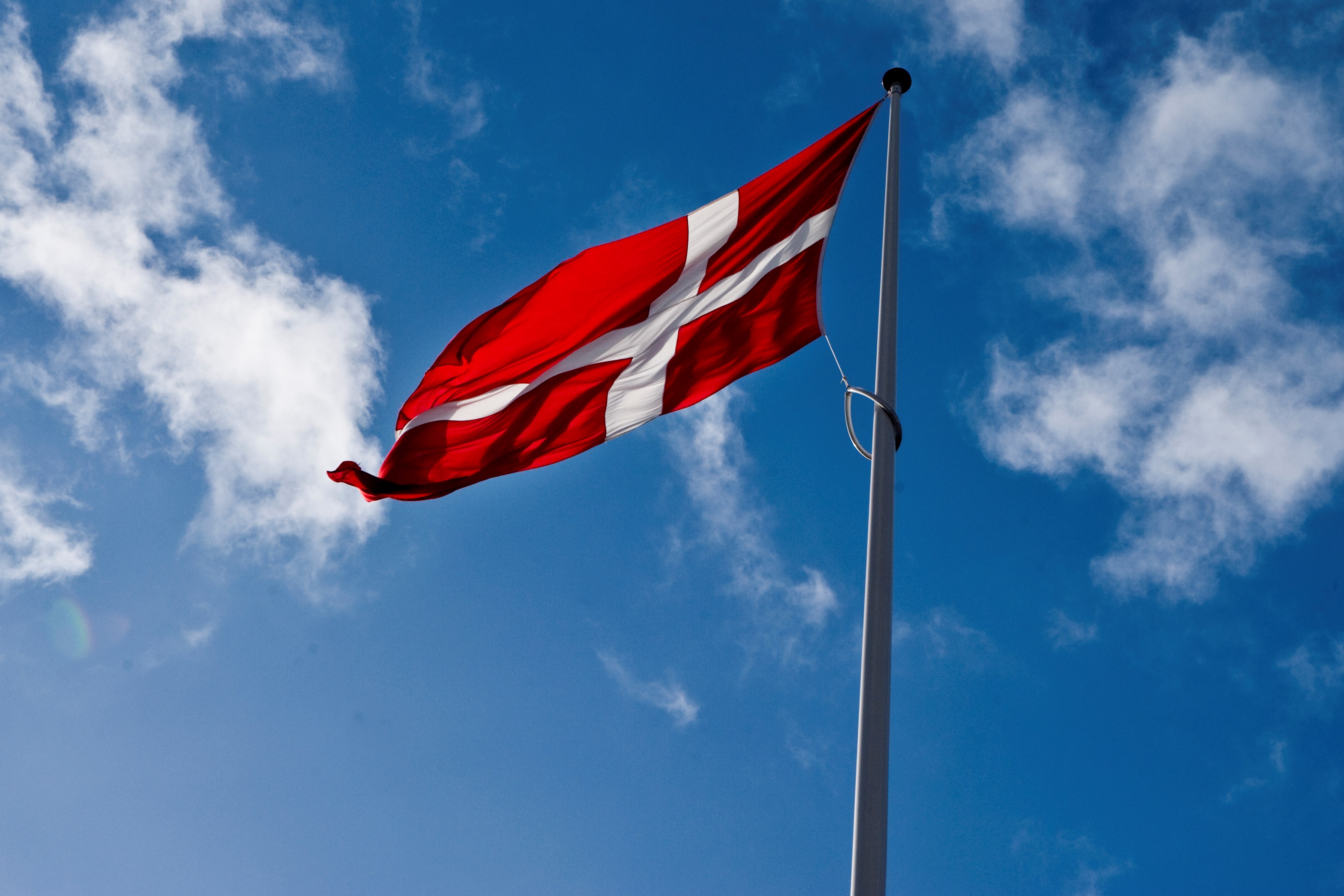 Dannebrogsflag til vejrs i flagstang med blå himmel og lette skyer