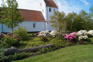 Næsbyhoved Broby kirke set udefra med grønne træer og bed med blomster